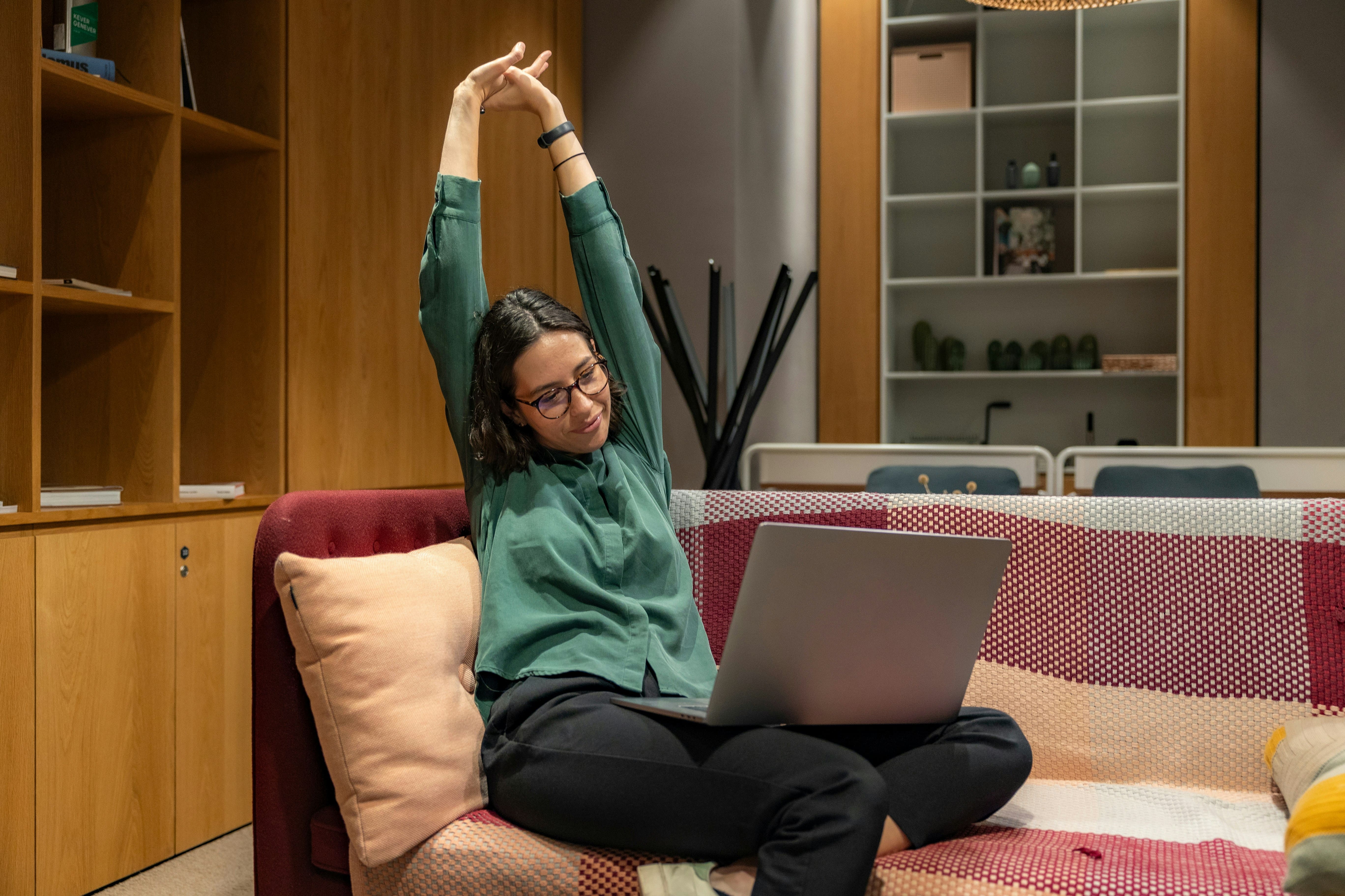 En glad kvinna sträcker på sig och ler medan hon arbetar på sin laptop i ett mysigt rum